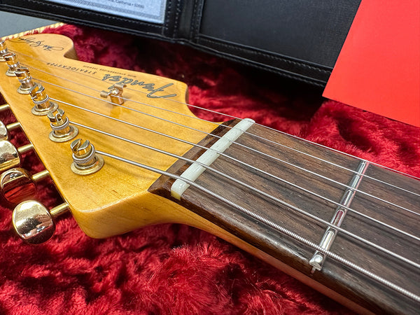 Close-up of Fender Stratocaster electric guitar headstock with gold tuning pegs and rosewood fretboard in red plush guitar case