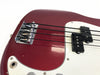 Close-up of red electric bass guitar body showing bridge, black pickups, white pickguard, and strings
