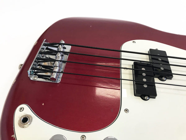 Close-up of red electric bass guitar body showing bridge, black pickups, white pickguard, and strings