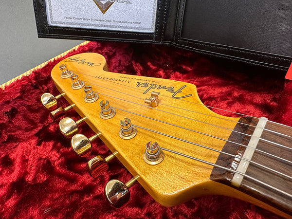 Close-up of Fender Stratocaster guitar headstock with gold tuning pegs and rosewood fretboard in red plush case lining