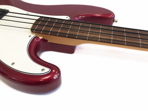 Close-up of red electric bass guitar body with white pickguard and brown fretboard with metal strings against white background