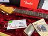 Close-up of Fender guitar neck with tuning pegs, Fender owner's manual, tremolo springs instructions, guitar picks, and Fender inspection tag on red plush guitar case lining