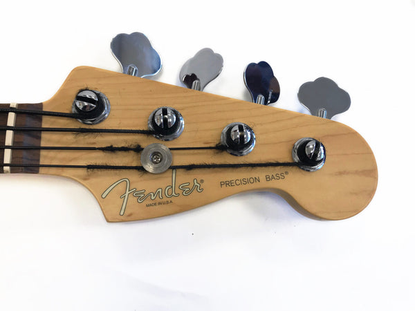 Close-up of Fender Precision Bass headstock with tuning pegs and strings on natural wood finish, made in USA.