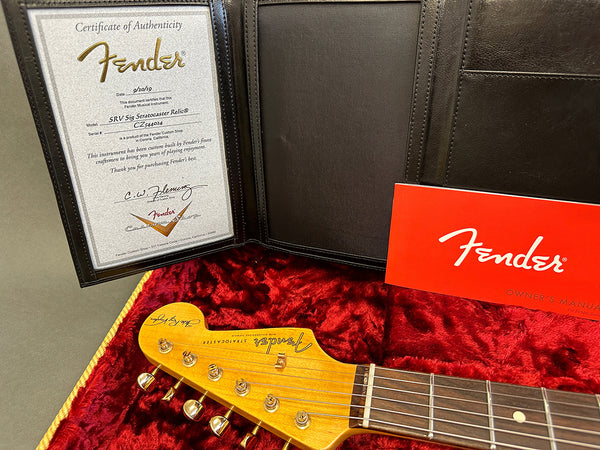 Fender SRV Signature Stratocaster Relic guitar headstock with certificate of authenticity and red Fender owner's manual displayed on red plush case lining