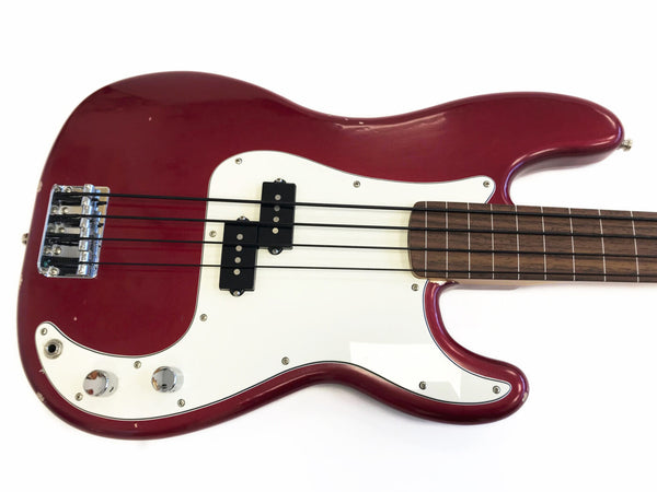 Red electric bass guitar with white pickguard and four strings on wooden fingerboard isolated on white background