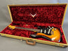Vintage Fender Stratocaster electric guitar in sunburst finish with black pickguard and signature etched design, displayed inside open tweed hard case with red plush interior lining.