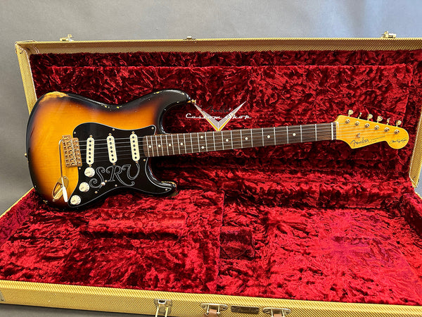 Fender Stratocaster SRV signature electric guitar in sunburst finish with black pickguard and white pickups, displayed in red plush-lined tweed hard case