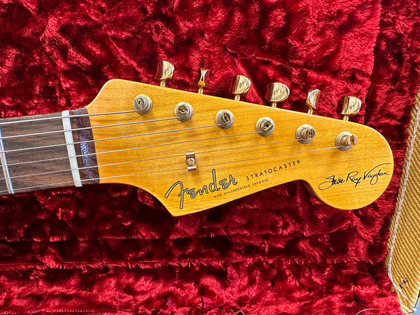Fender Stratocaster guitar headstock with vintage gold tuning pegs and "Jimi Ray Vaughan" signature on red plush case background