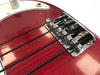 Close-up of red electric bass guitar bridge and black strings with chrome hardware and white pickguard edge visible