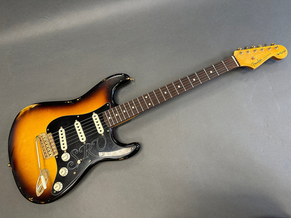 Vintage Fender Stratocaster electric guitar with sunburst finish, black pickguard engraved with "SRV," three single-coil pickups, rosewood fretboard, and signed headstock.