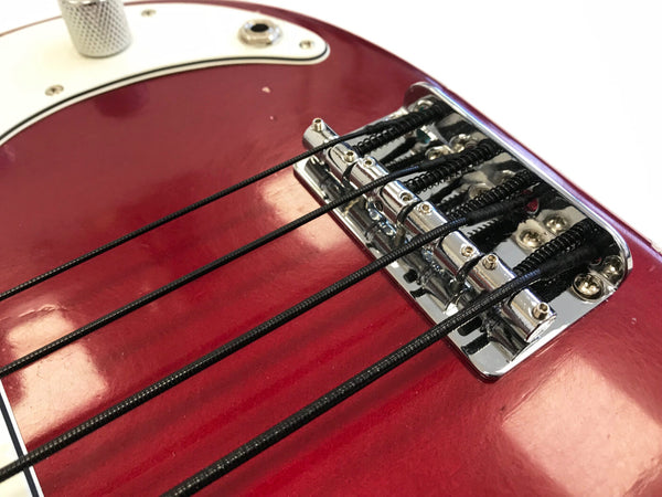 Close-up of red electric bass guitar bridge and black strings with chrome hardware and white pickguard edge visible