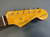 Close-up of Fender Stratocaster guitar headstock with gold tuning pegs and rosewood fretboard on gray background