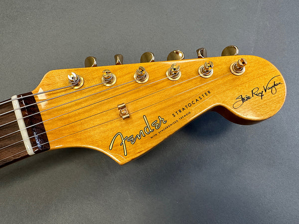 Close-up of Fender Stratocaster guitar headstock with gold tuning pegs and rosewood fretboard on gray background