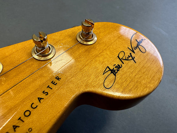 Close-up of Fender Stratocaster guitar headstock with gold tuning pegs and Stevie Ray Vaughan signature on natural wood finish