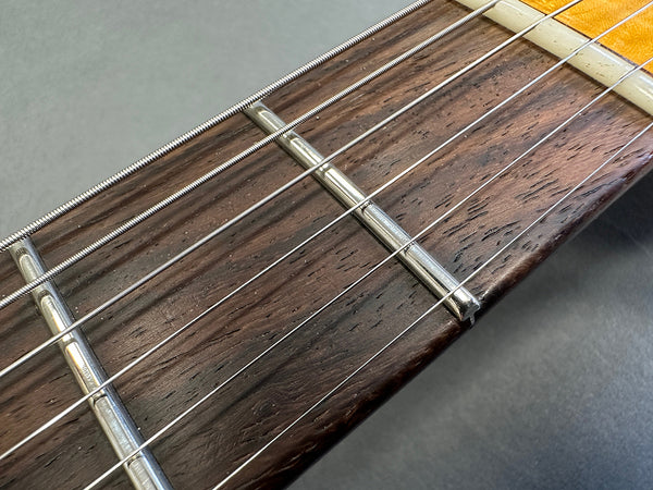Close-up of guitar fretboard with metal frets and steel strings on dark wood fingerboard