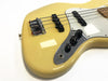 Close-up of cream-colored electric bass guitar body with chrome bridge, black pickups, white pickguard, and three black control knobs on reflective control plate