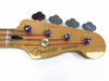 Close-up of Fender Precision Bass headstock with tuning pegs and red-wrapped bass strings on natural wood finish