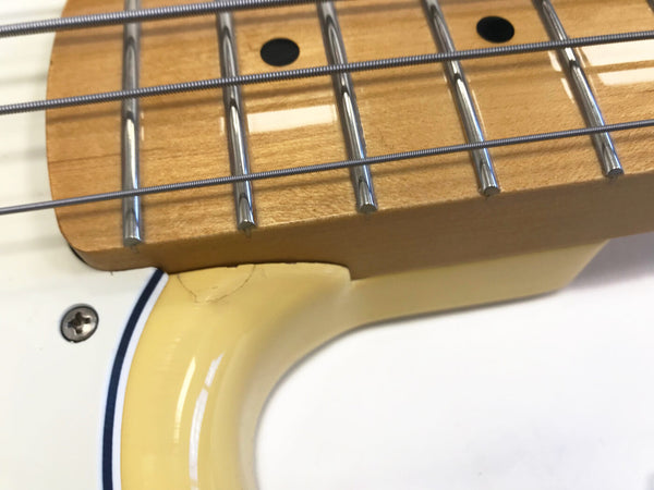 Close-up of maple fretboard with metal frets and four strings on white electric guitar body showing neck joint area with yellow tint and screw detail.