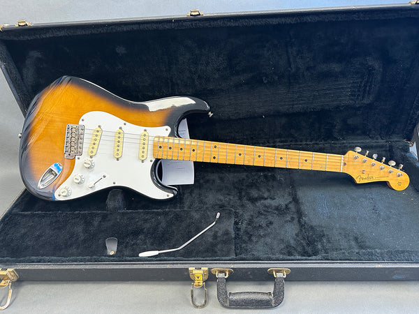 Fender Stratocaster electric guitar with sunburst finish, maple neck, and three single-coil pickups in black hard case with tremolo arm and control knobs visible