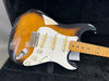 Sunburst electric guitar with maple fretboard, three single-coil pickups, white pickguard, volume and tone knobs, inside black guitar case