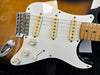Close-up of electric guitar body with sunburst finish, white pickguard, three single-coil pickups, volume and tone control knobs, and tremolo bridge