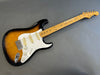 Fender Stratocaster electric guitar with sunburst finish, maple neck, and white pickguard on gray background.