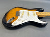 Sunburst electric guitar with white pickguard and maple neck on gray surface