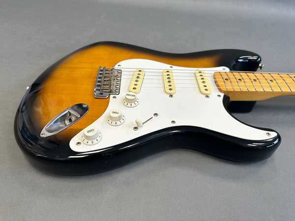 Sunburst electric guitar with white pickguard and maple neck on gray surface
