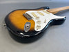 Sunburst electric guitar with white pickguard and three single-coil pickups on gray background