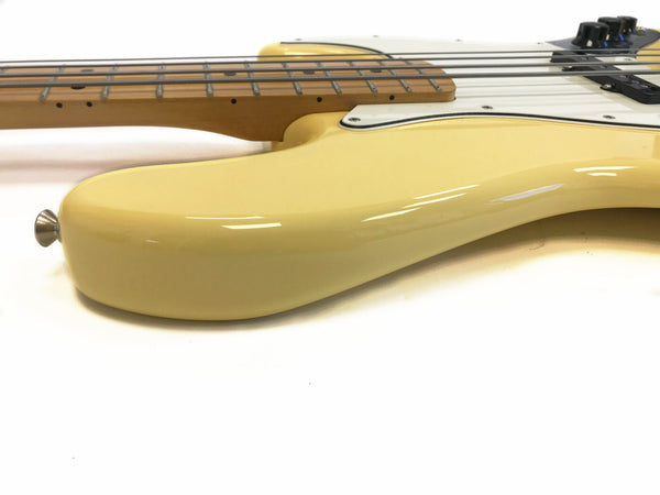Close-up of cream-colored electric bass guitar body and maple neck with fretboard and black control knobs on white background