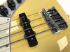 Close-up of yellow electric bass guitar bridge, pickups, and strings with black control knobs and chrome hardware
