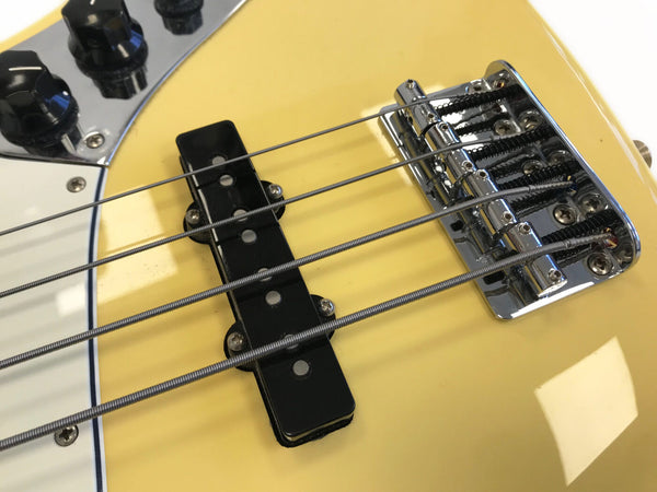 Close-up of yellow electric bass guitar bridge, pickups, and strings with black control knobs and chrome hardware