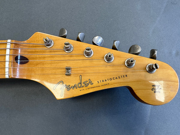 Close-up of Fender Stratocaster guitar headstock with six tuning pegs and natural wood finish on Gray background