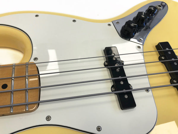 Close-up of yellow electric bass guitar body showing white pickguard, black pickups, metal strings, and control knobs