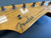 Close-up of Fender Stratocaster headstock with tuning pegs and strings on natural wood finish guitar