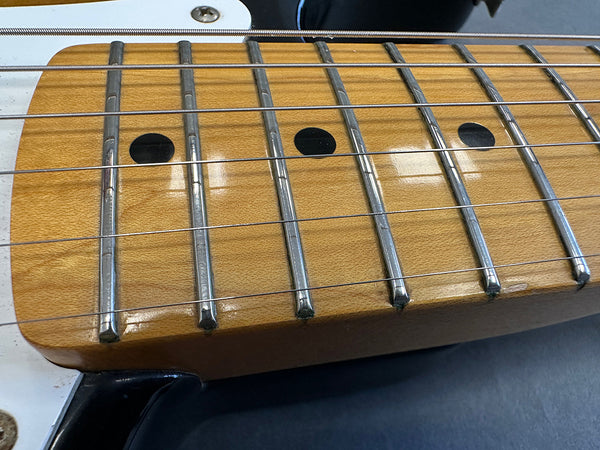 Close-up of maple guitar neck with metal frets and black dot inlays on electric guitar fretboard