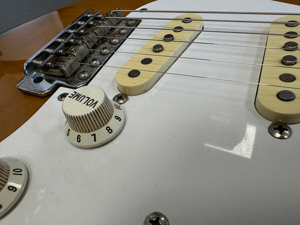 Close-up of white electric guitar volume knob, cream single-coil pickups, and rusty metal bridge on brown body guitar surface