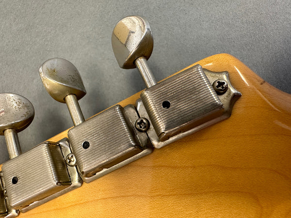 Close-up of vintage metal tuning pegs on the back of a light wood electric guitar headstock against a gray background