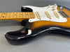 Close-up of sunburst electric guitar body and maple neck with white pickguard and three single-coil pickups on gray background