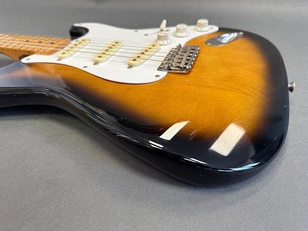 Sunburst finish electric guitar body with white pickguard and three single-coil pickups on gray background