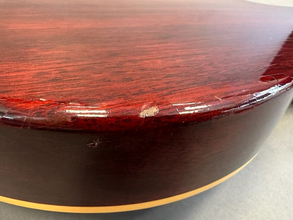 Close-up of worn and chipped edge on red vintage acoustic guitar body with glossy finish and cream binding