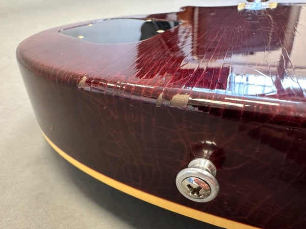 Close-up of worn red electric guitar body with scratches and finish chips near strap button and cream binding