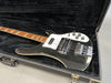 Black electric bass guitar with white pickguard in open black hard case on gray surface