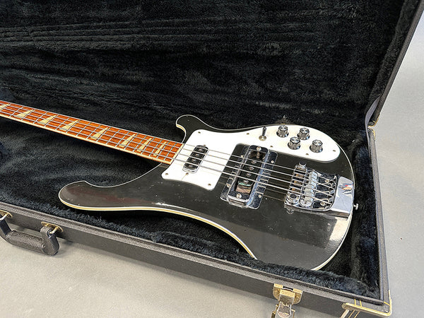 Black electric bass guitar with white pickguard in open black hard case on gray surface