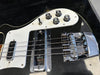 Close-up of black electric bass guitar body showing chrome bridge, pickups, and control knobs on white pickguard.
