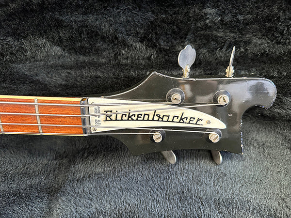 Close-up of Rickenbacker electric bass guitar headstock with tuning pegs and visible strings on black textured background