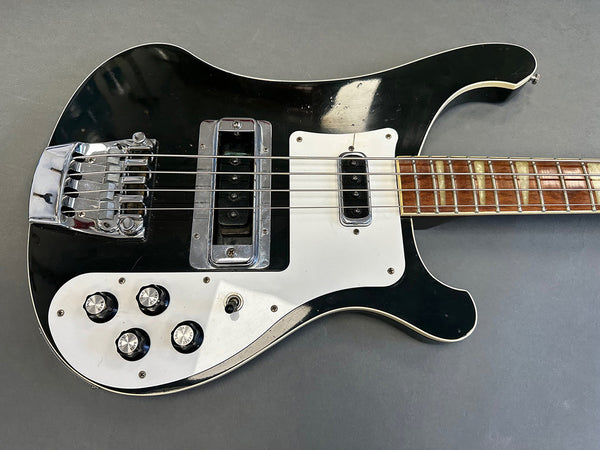 Black and white electric bass guitar with chrome bridge, four control knobs, toggle switch, and rosewood fretboard on grey background