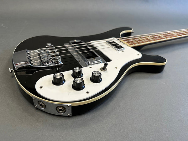 Black and white electric bass guitar with chrome hardware and four control knobs on grey background