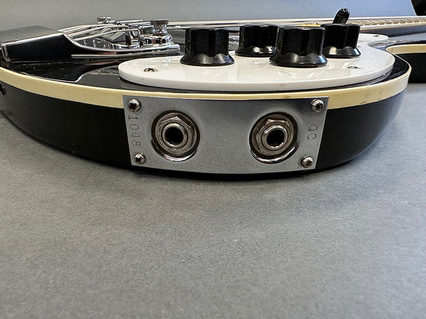 Close-up of black and white electric guitar side panel showing dual audio output jacks and control knobs on gray surface