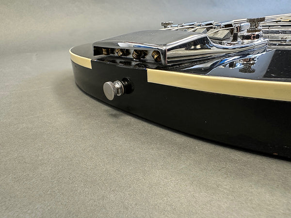 Close-up of black electric guitar body with cream binding and chrome tailpiece showing strap button and bridge hardware at Coffee House Guitars.